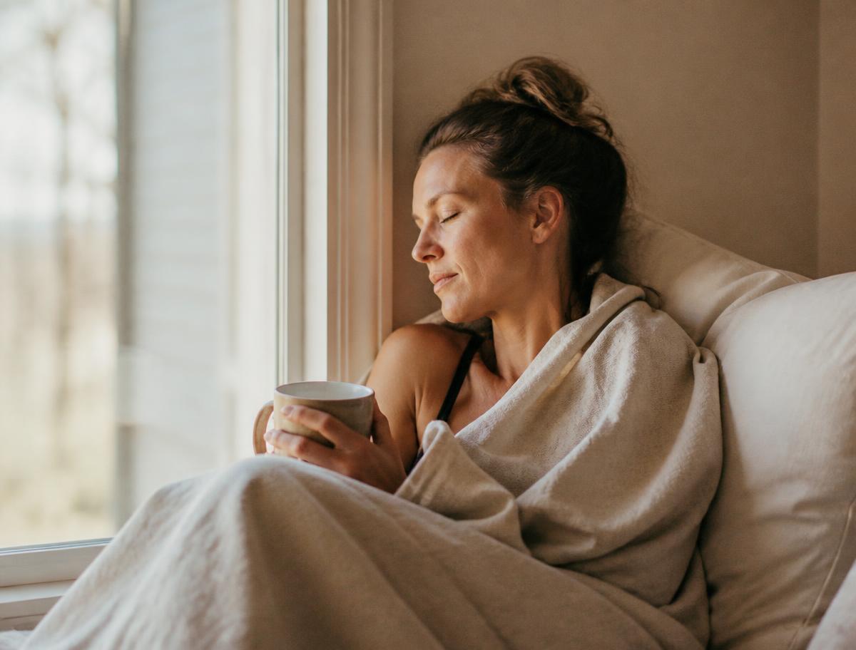 A mother resting by a window wrapped in a blanket